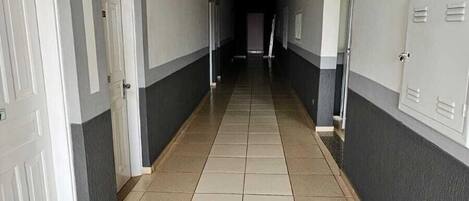 A long, narrow hallway with white and gray walls, a tiled floor, and doors on both sides.