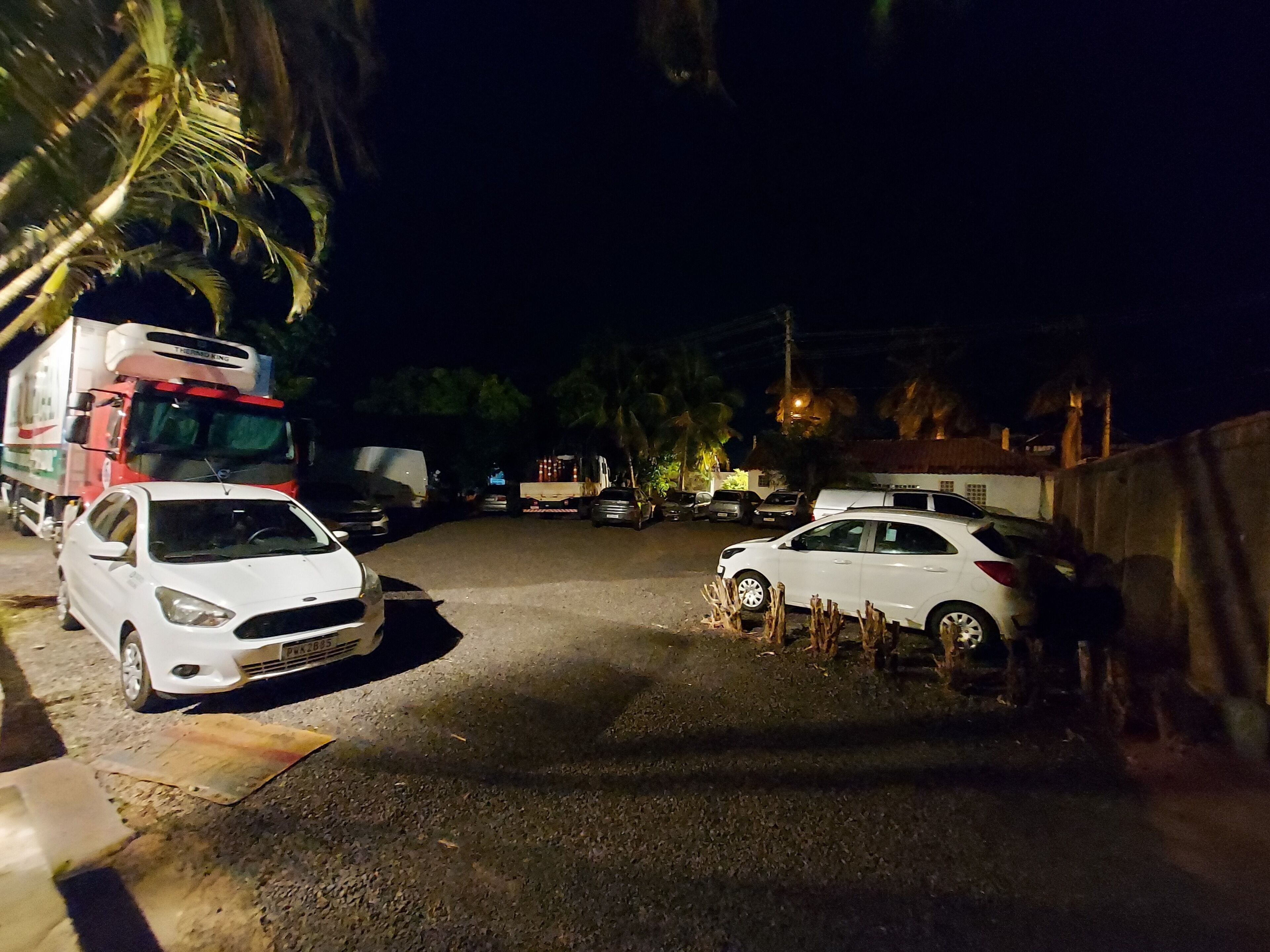 A nighttime parking area with several cars and a large truck.