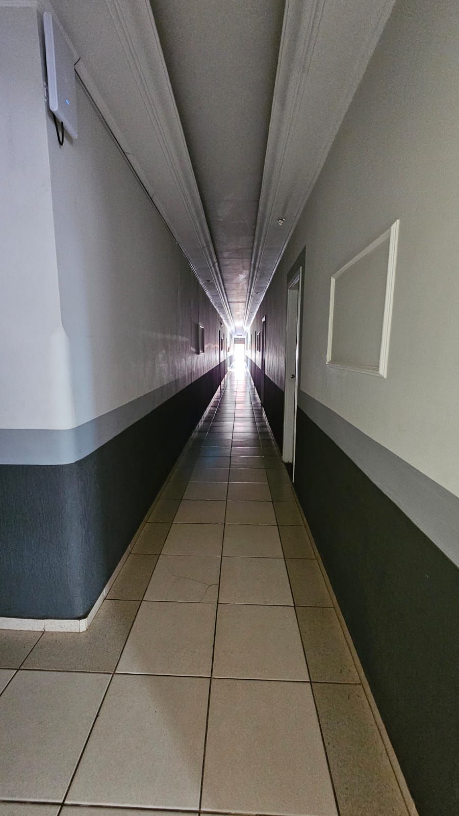 A long, narrow hallway with tiled floors and walls, leading to a bright exit at the end.