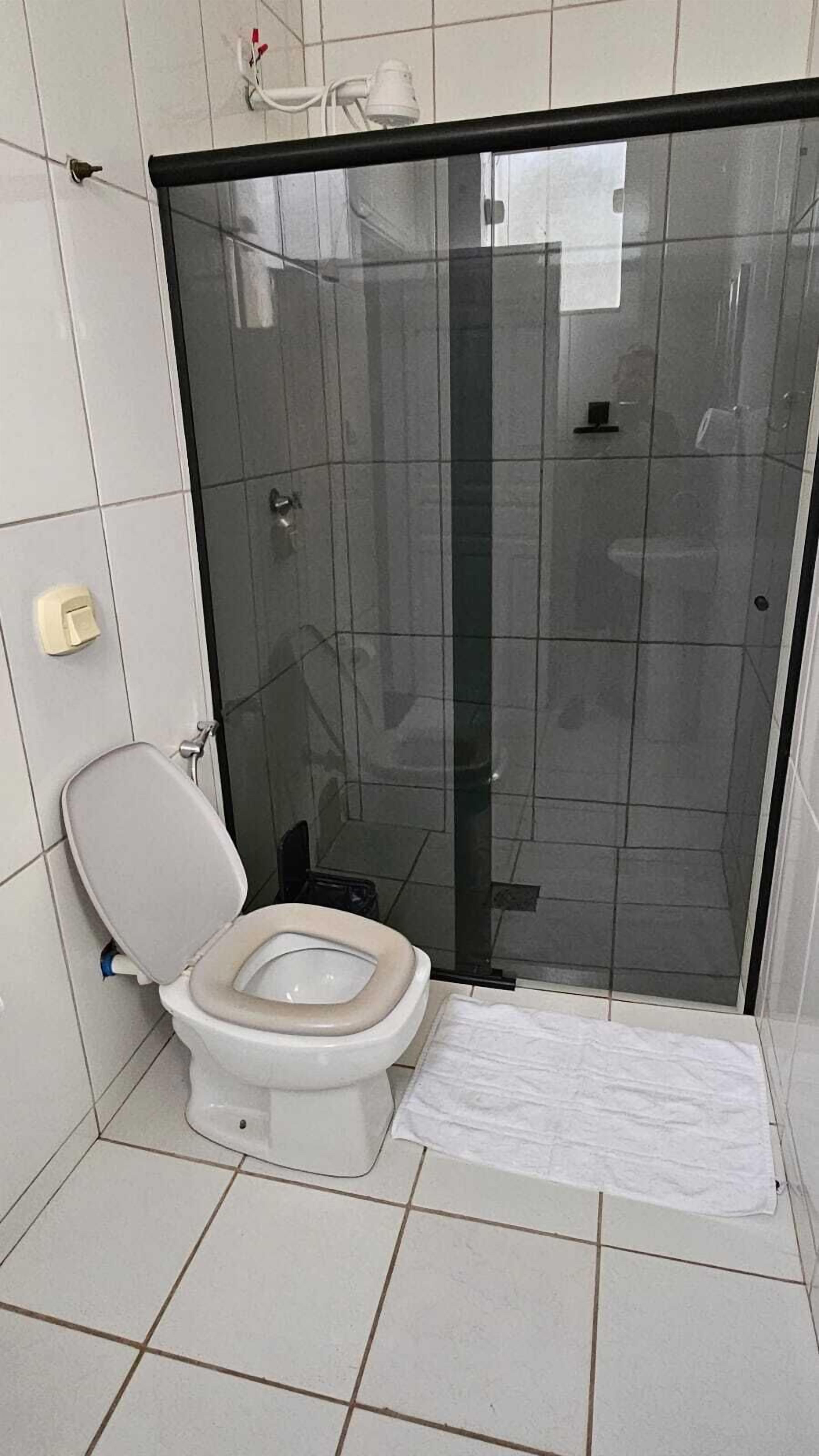 Un baño con inodoro, ducha con mampara de vidrio y una toalla blanca en el suelo.