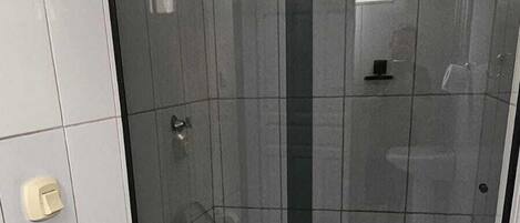 Un baño con inodoro, ducha con mampara de vidrio y una toalla blanca en el suelo.