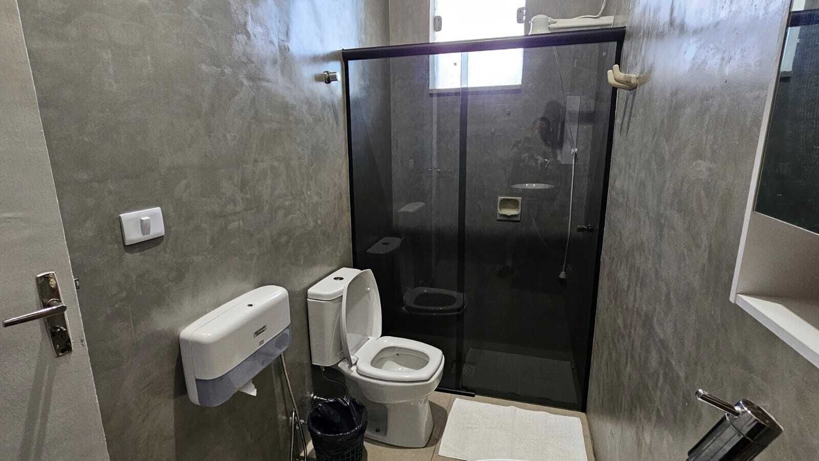A modern bathroom with a toilet, a hand dryer, a trash bin, and a glass-enclosed shower area.