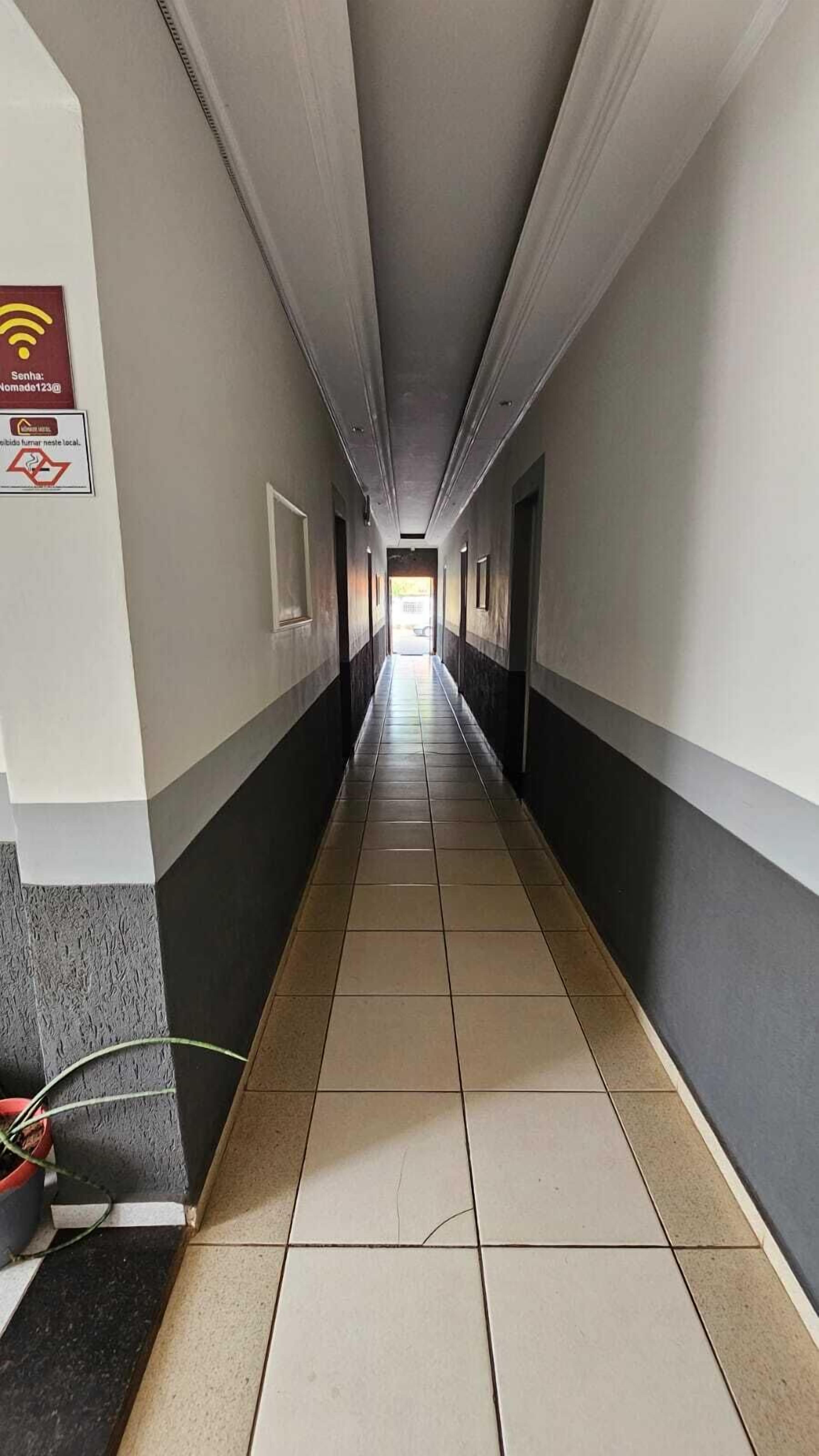 Un pasillo largo y estrecho con pisos y paredes de baldosas, que conduce a una zona luminosa al final.