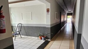 Ένας διάδρομος με πλακάκια στο δάπεδο, ένας πυροσβεστήρας, μια καρέκλα και μια γλάστρα με φυτό.