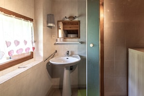A bathroom with a sink, mirror, towel rack, and a window with heart-shaped decorations.