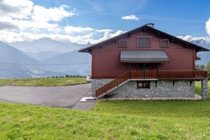 Une maison en bois rouge, avec des fondations en pierre, un balcon en bois et une allée pavée.