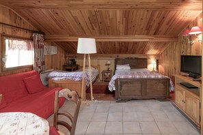A wooden cabin bedroom with two beds, a red sofa, a television, and a lamp.