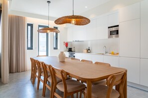 Una cocina moderna con armarios blancos, una mesa de comedor de madera y lámparas colgantes de mimbre.