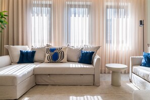 A beige sectional sofa with blue and white patterned pillows, a round white side table, and sheer curtains. - Feel Porto Tawny Townhouse (Porto)