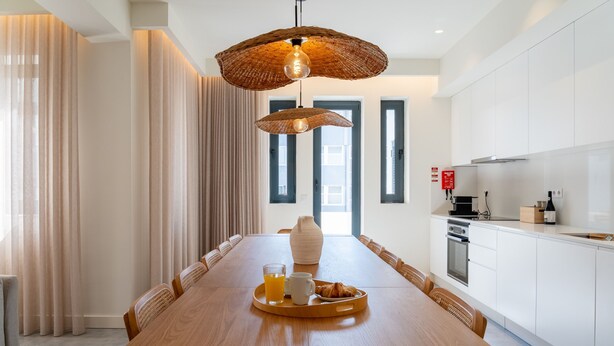 Un espace repas moderne avec une table en bois, un luminaire suspendu en fibres tressées et un plateau de petit-déjeuner.