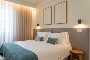 Una habitación de hotel con cama, mesita de noche, lámpara y ventana con cortinas.