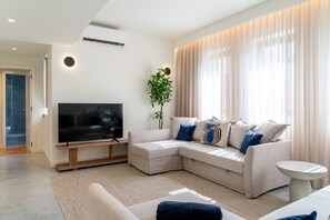 A modern living room with a sectional sofa, a flat-screen TV, a small side table, and a potted plant.