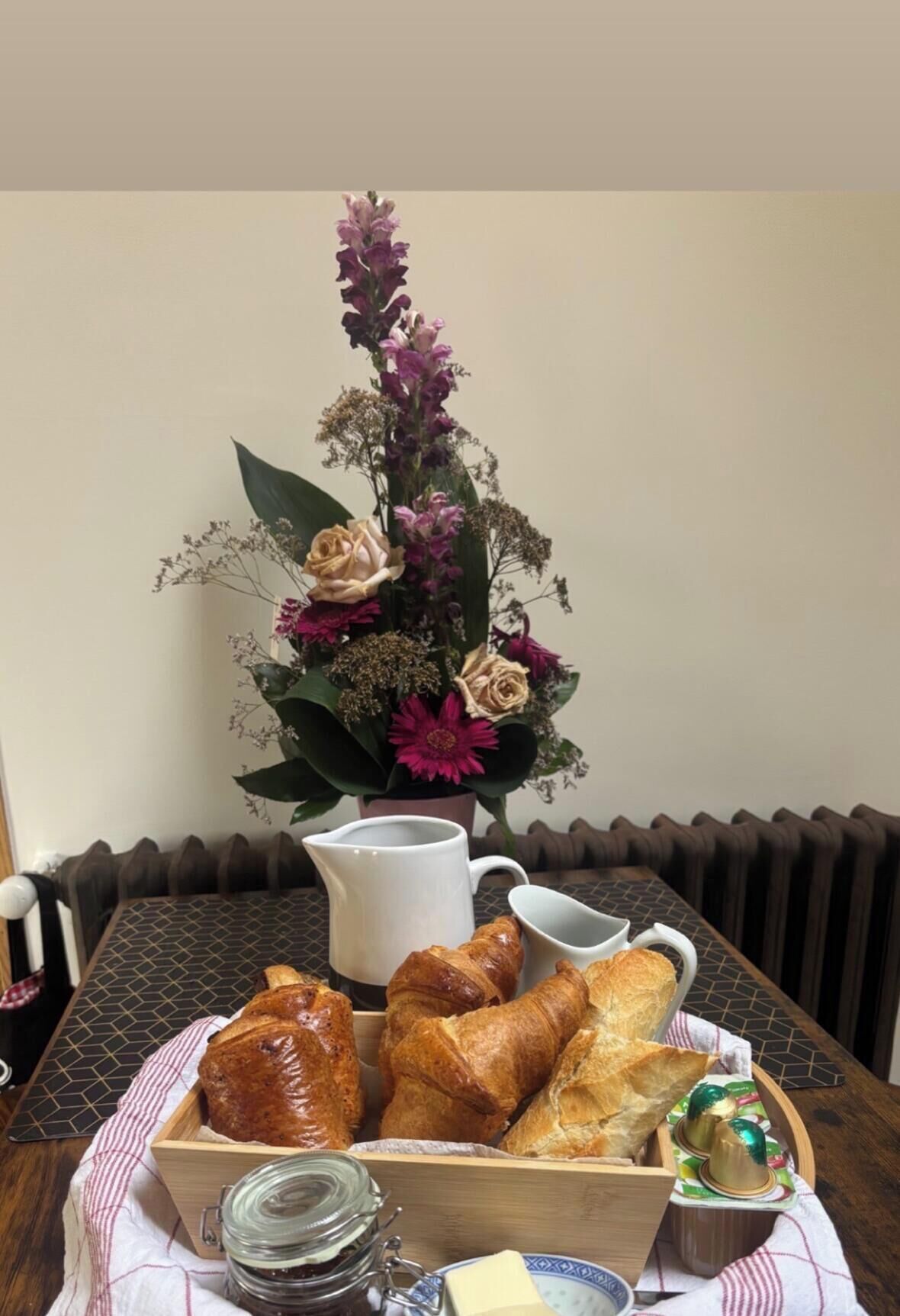 A dining table with a floral centerpiece, a pitcher, and a tray of pastries.