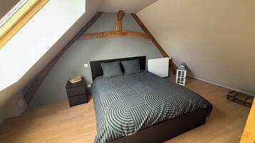 Un dormitorio con techo inclinado, una cama con colcha estampada, una mesita de noche con lámpara y un radiador.