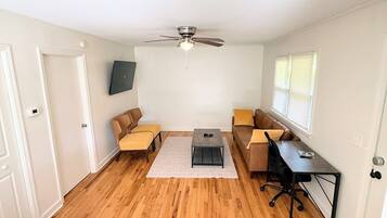 A spacious room with hardwood flooring, a ceiling fan, two sofas with cushions, a small coffee table, and a desk with a chair.