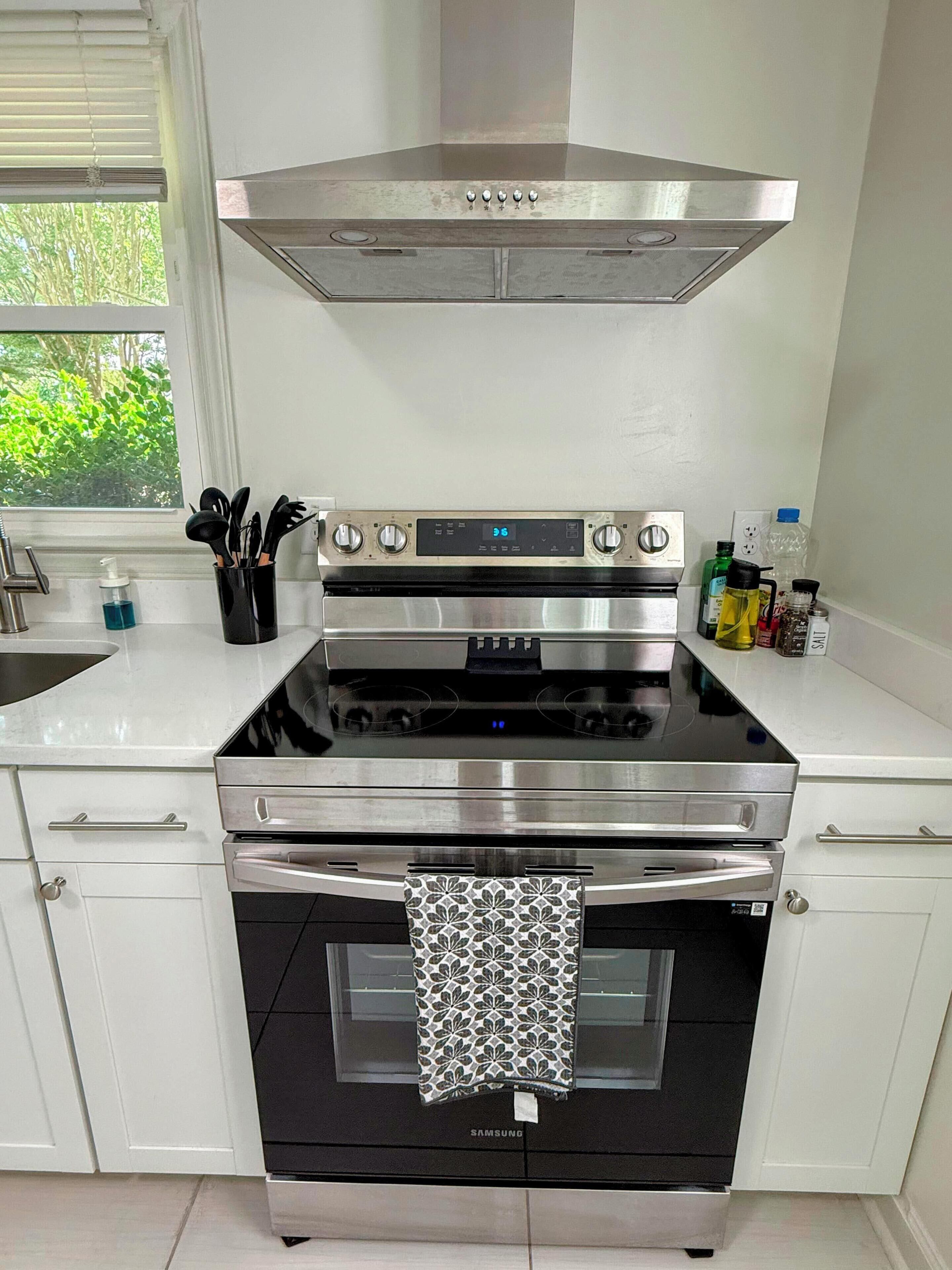 Una cocina con extractor de acero inoxidable, horno empotrado y microondas.