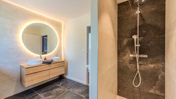 A modern bathroom with a round mirror, two sinks, a wooden vanity, and a shower with a handheld showerhead.