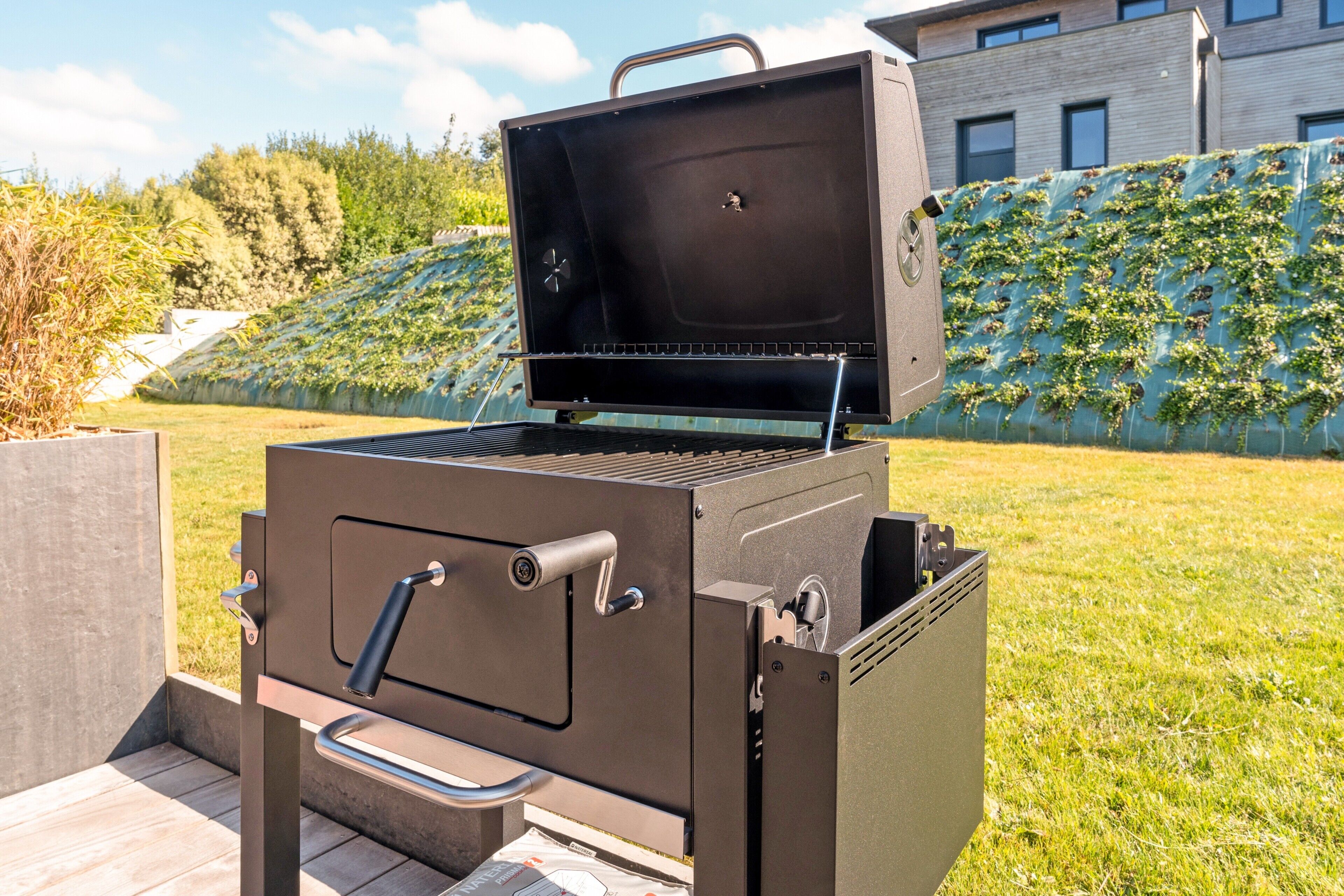Una parrilla moderna para exteriores con un asa y perillas de control, sobre una terraza de madera.