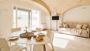 Un espace repas comprenant une table ronde, des chaises et un buffet garni de pain et d’olives.