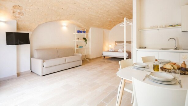 Un espace de vie moderne comprenant un canapé, une table à manger pour deux personnes et un coin cuisine.