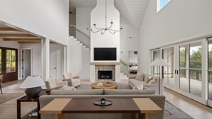 Amplia sala de estar con chimenea, televisor grande y techo alto con vigas a la vista.