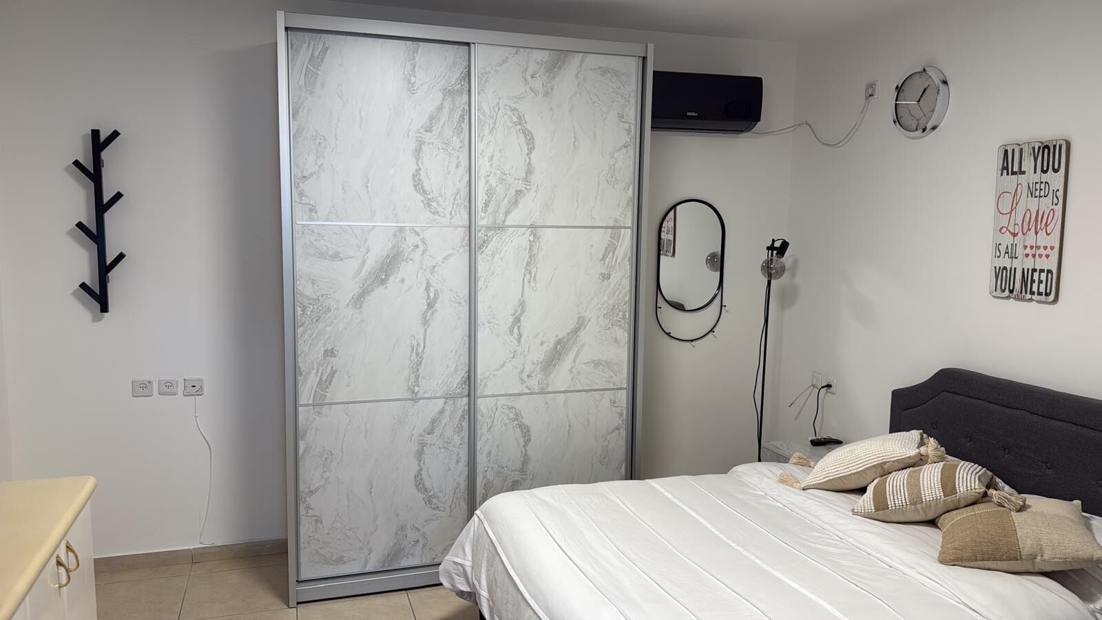 Een slaapkamer met een bed, een kledingkast, een spiegel en een muur met een motiverende quote.
