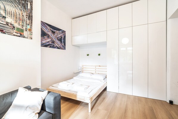 A modern bedroom with a bed, a grey sofa, and a wardrobe.