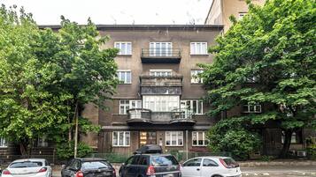 Un immeuble à plusieurs étages doté d’une entrée centrale, de balcons et de voitures garées devant.