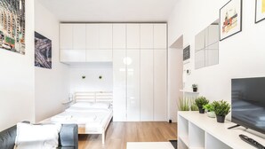 A modern, compact hotel room with a bed, a sofa, a TV, and a small balcony with plants. - ShortStayPoland Józefitów C4 (Kraków)