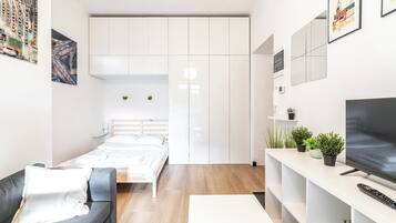 Une chambre d’hôtel moderne et compacte, dotée d’un lit, d’un canapé, d’une télévision et d’un petit balcon agrémenté de plantes.