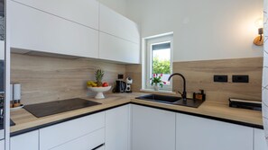 Une cuisine moderne avec des meubles blancs, un plan de travail en bois, un évier noir et une fenêtre donnant sur un espace verdoyant.