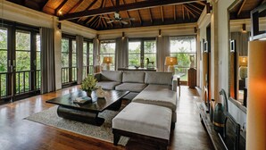 A spacious living room with a large sectional sofa, a coffee table, and a fireplace. There are large windows providing natural light and views of greenery outside. - Specious  three bedrooms villa in beautiful Jimbaran with private pool (Bali)