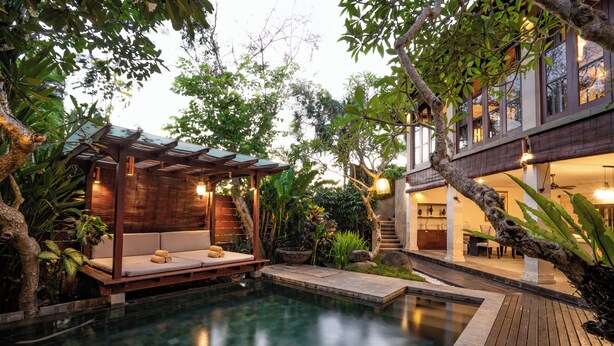 A serene outdoor pool area with a wooden deck, a seating area with cushions, and a pergola with lights. - Specious  three bedrooms villa in beautiful Jimbaran with private pool (Bali)