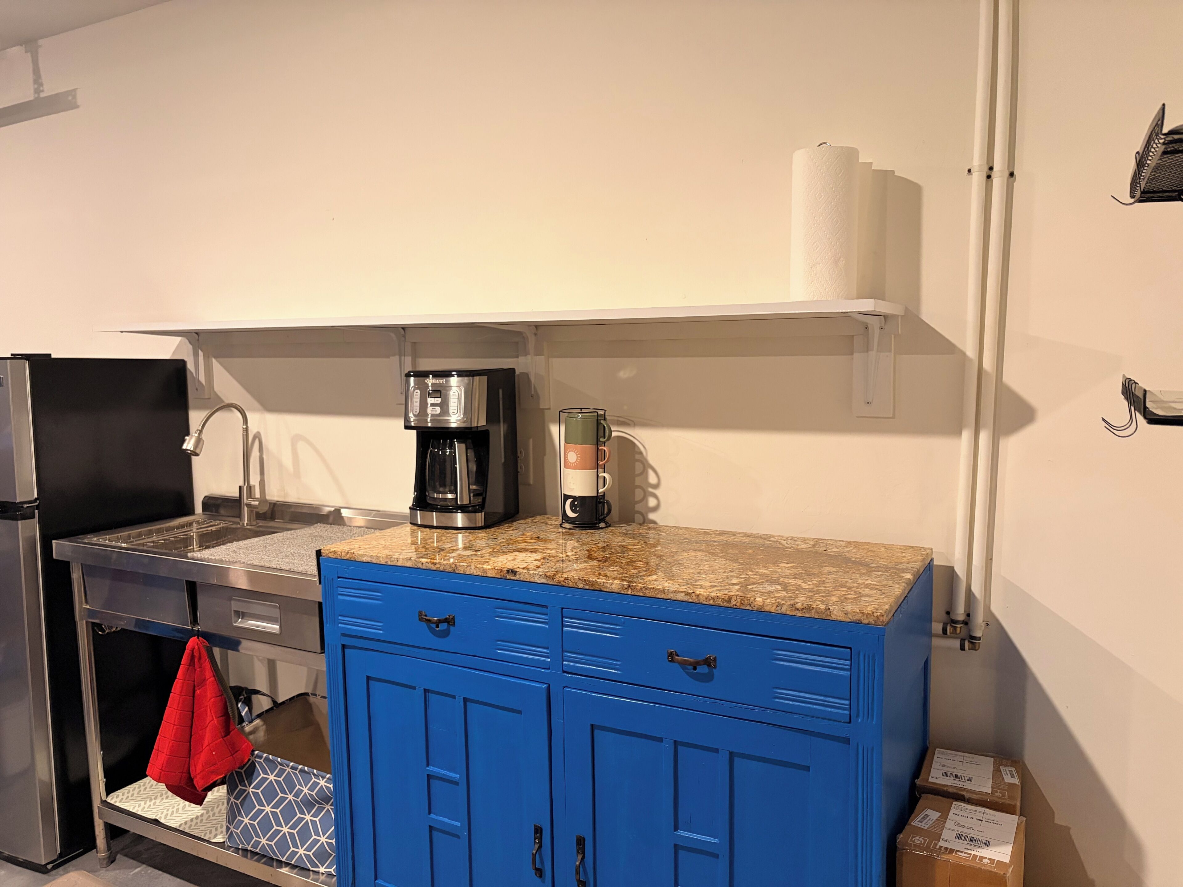 Una cocina compacta con cafetera, lavamanos y un armario azul.