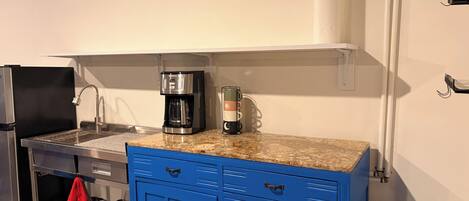 Una cocina compacta con cafetera, lavamanos y un armario azul.