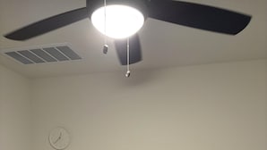 Une chambre à coucher avec un lit, un ventilateur de plafond, une horloge murale et une petite table sur laquelle est posée une plante.