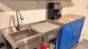 Une cuisine équipée d’un évier en acier inoxydable, d’une machine à café et de meubles de rangement bleus.