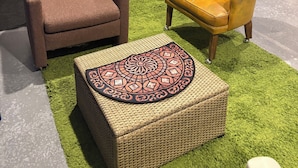 Une pièce avec un fauteuil marron, un fauteuil jaune avec un coussin et un pouf en osier sur un tapis vert.