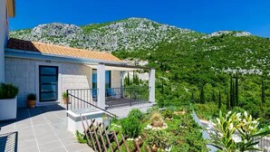 Una casa moderna con techo de tejas, balcón y jardín con diversas plantas.