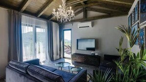 Una sala de estar con sofá, televisor, candelabro y vista al exterior.