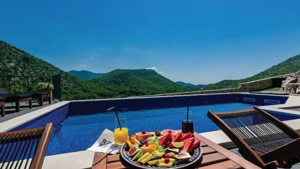 Desayuno junto a la piscina con una variedad de frutas y bebidas, con vistas a un paisaje montañoso.