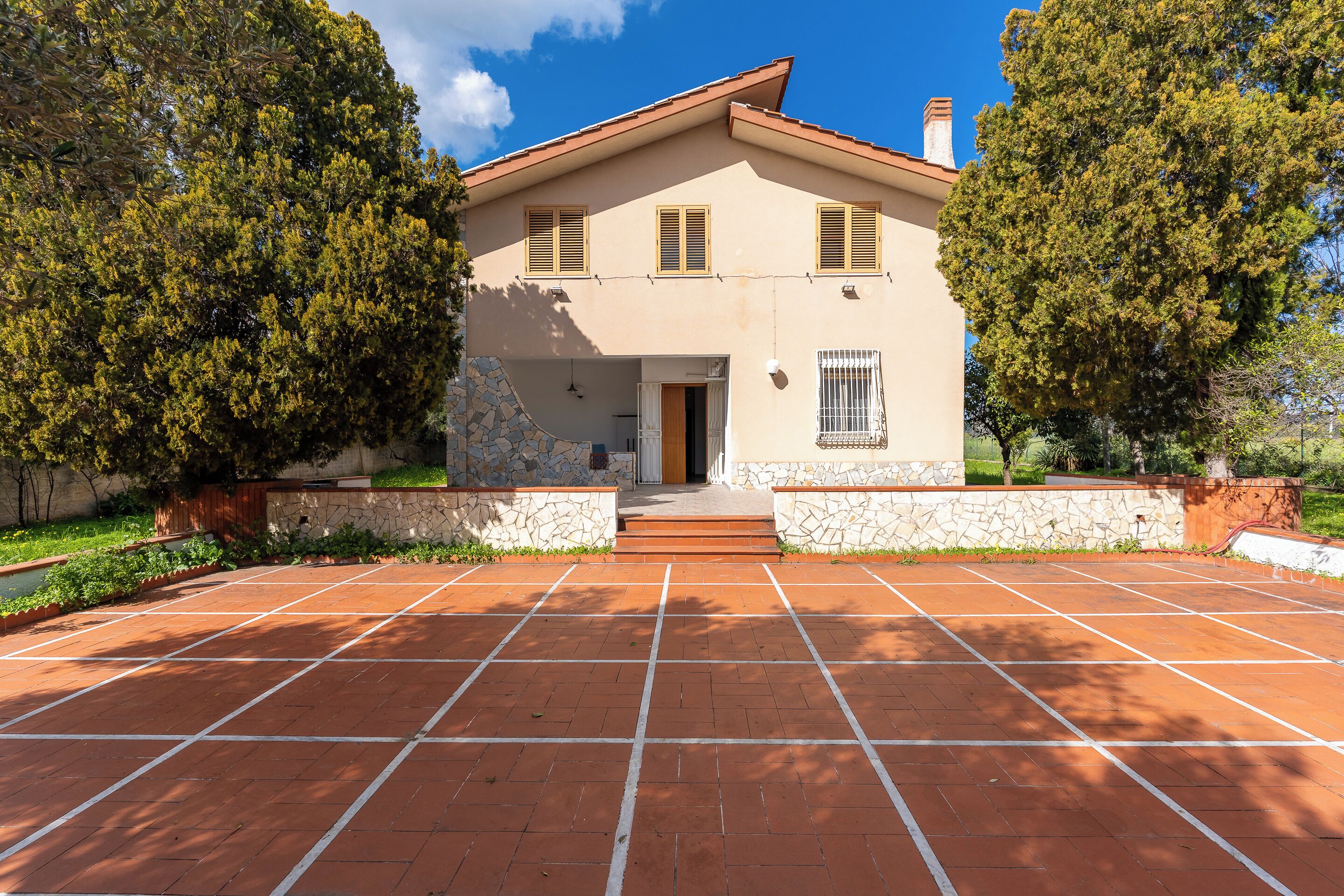 A two-story house with a tiled driveway and stone walls.