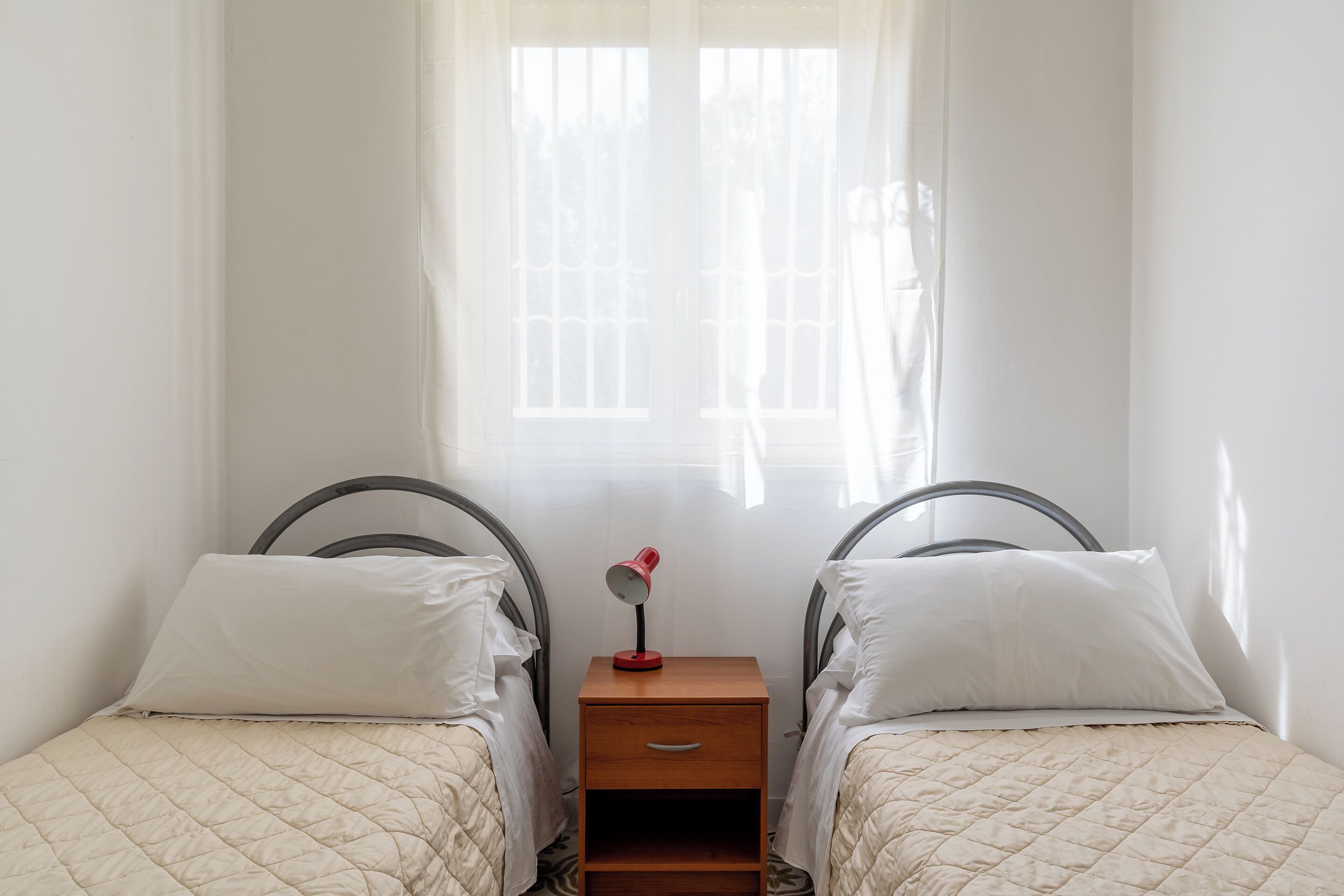 A twin bedroom with two beds, a nightstand, and a window with curtains.