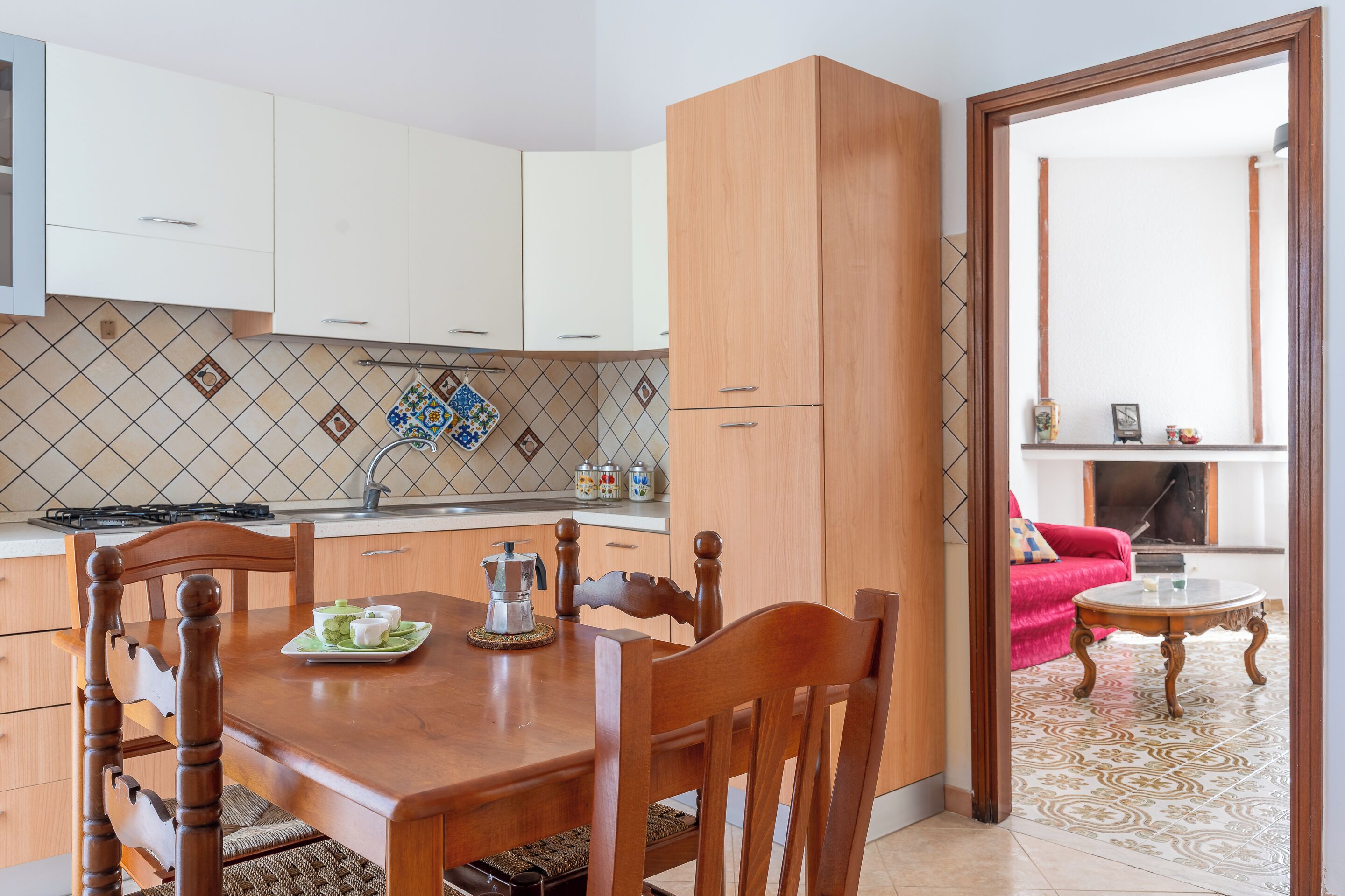 A modern kitchen with white cabinets, a wooden dining table, and a red sofa in the living area.