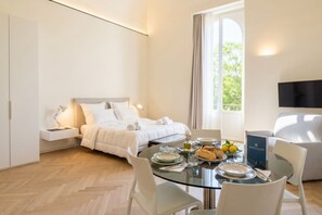 A modern hotel room with a bed, a dining table with plates and glasses, a TV, and a window with curtains. - Palazzo della Torre 102 - Luxury modern suite (Bari)