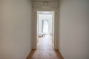 A hallway with a white door leading to a room with a bed and a chair.