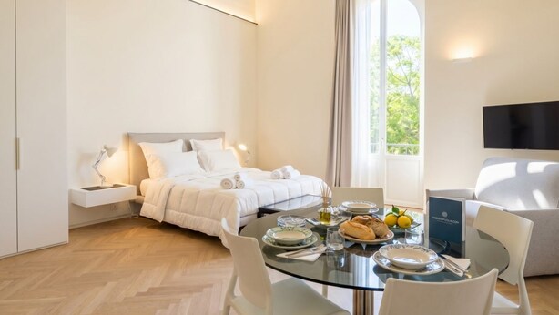 Una habitación de hotel moderna con una cama, una mesa de comedor con platos y vasos, un televisor y una ventana con cortinas.