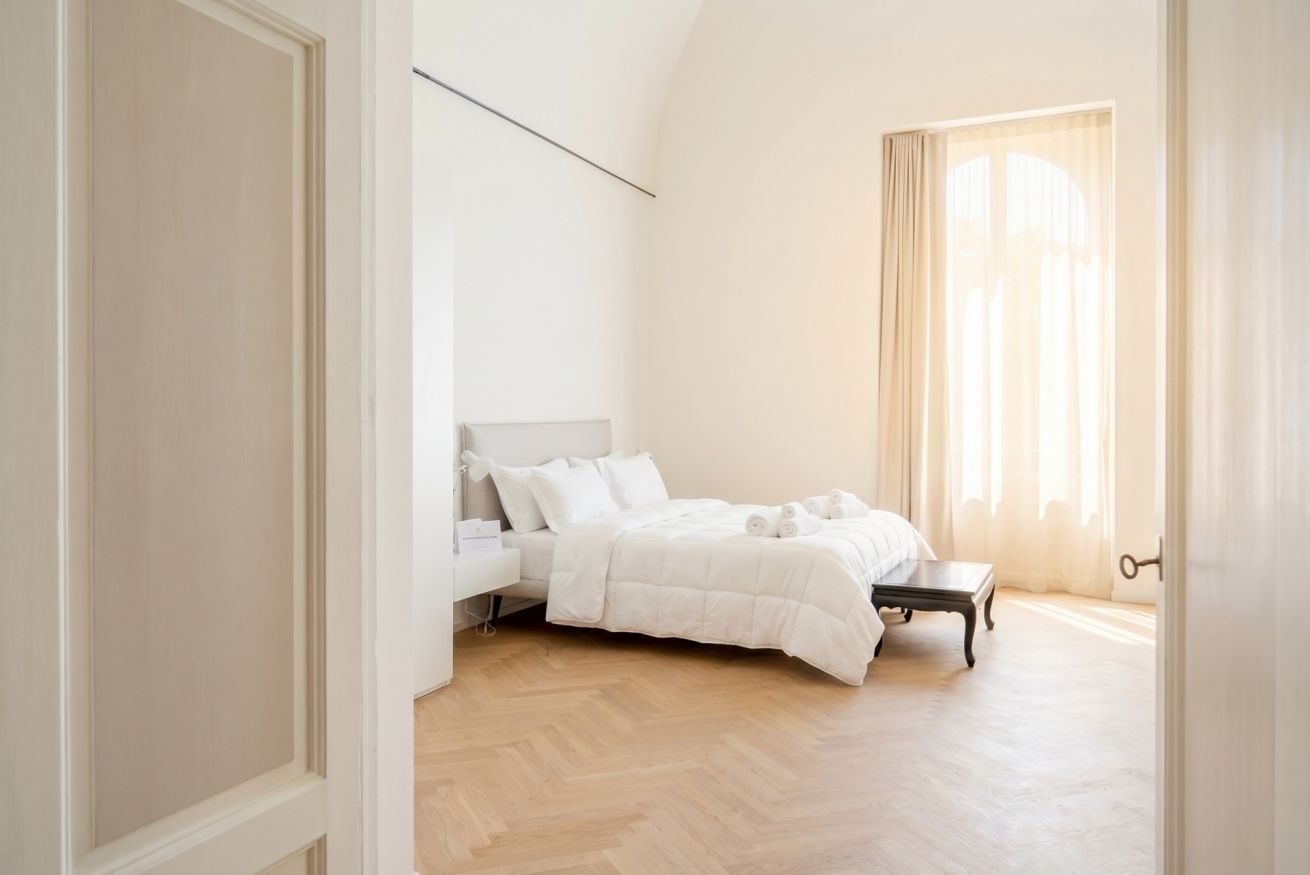 Ein Schlafzimmer mit einem Bett, einem Nachttisch, einem Fenster mit Vorhängen und einem Holzboden.