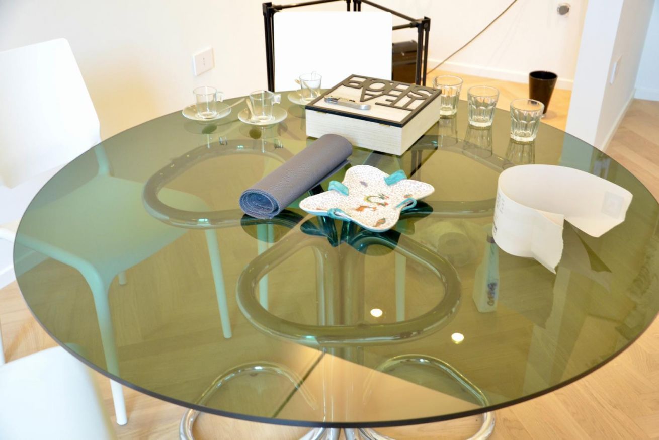 A round glass table with a book, glasses, and a rolled-up mat.