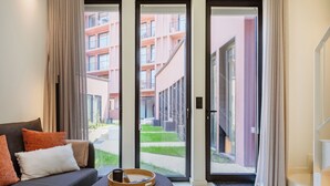 A modern hotel room with a sofa, a tray table, and a view of a courtyard and adjacent buildings. - Urban Loft at Terracotta Collection (Porto)
